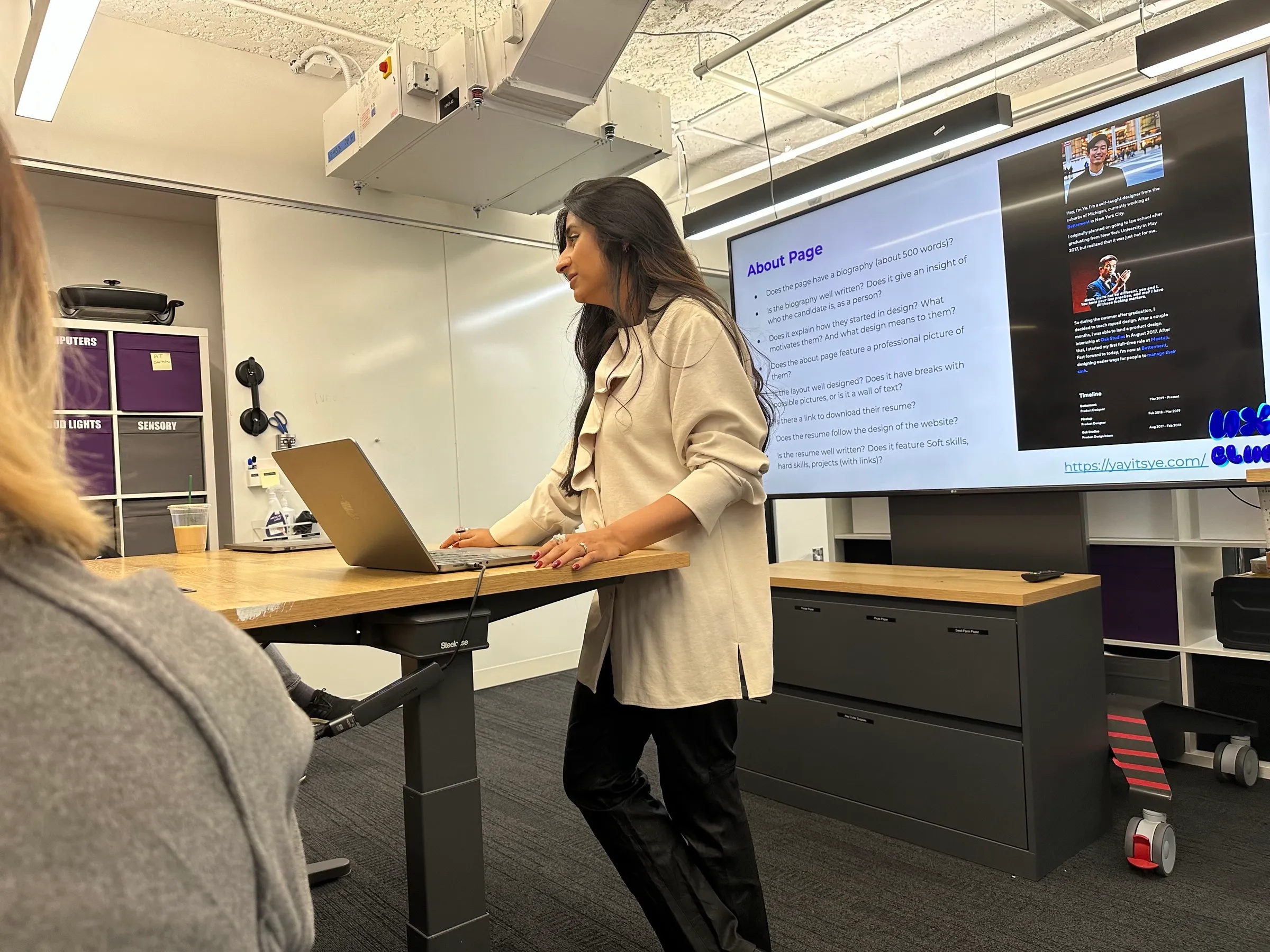 Sana presenting from a standing desk beside a projected slide